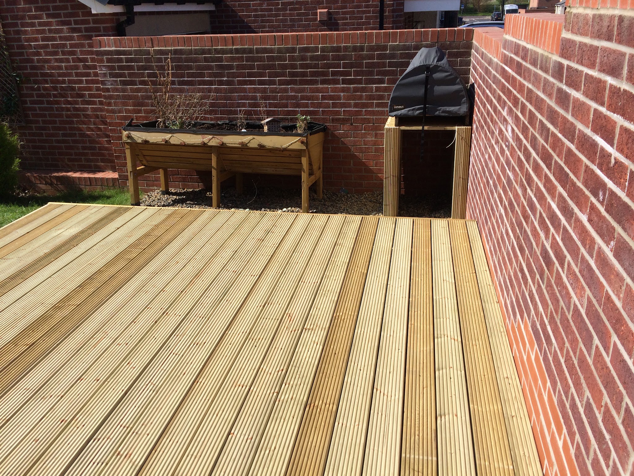 New decking against brick walls with a planter and barbecue